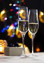 concept of celebrating christmas and new year, two glasses of champagne on the background of candles and colorful garlands, warm home traditional festive atmosphere