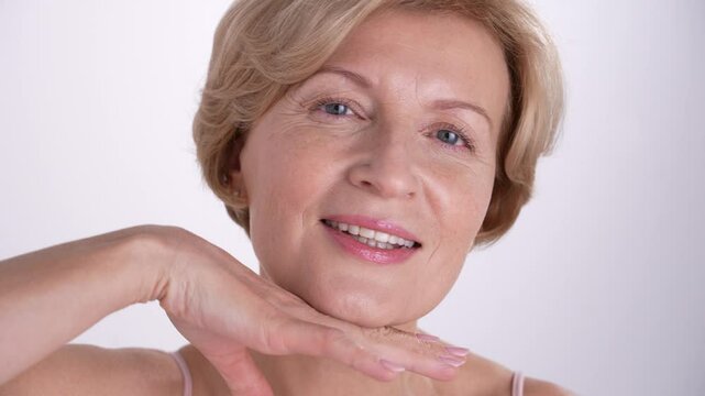 Closeup portrait of a confident woman in her 50s is gently touching her face, celebrating the beauty of graceful aging and selflove