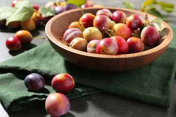 Ripe plums in bowl on grey table, closeup