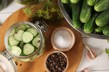 Homemade pickles. Fresh cucumbers in jar, dill and spices on white wooden table, flat lay