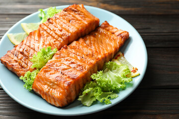 Delicious grilled salmon fillets with lettuce and lemon on wooden table, closeup