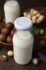 Bottle of macadamia milk and nuts on wooden table, closeup