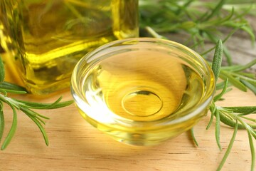 Cooking oil and rosemary on wooden table, closeup