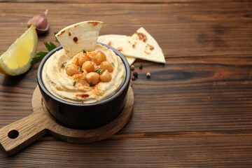 Delicious hummus with chickpeas and pita served on wooden table, space for text