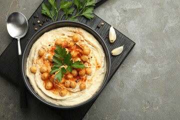 Delicious hummus with parsley, paprika and chickpeas on grey table, top view