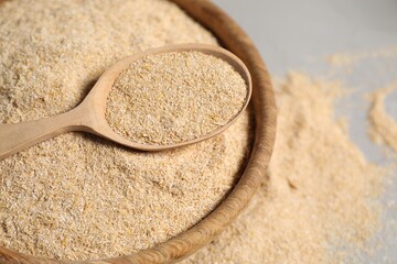 Oat bran in bowl and wooden spoon on table, closeup
