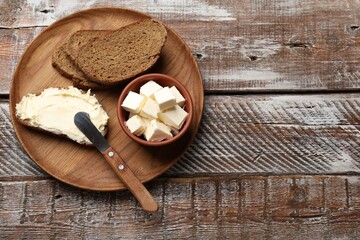 Fresh bread with butter and knife on wooden table, top view. Space for text