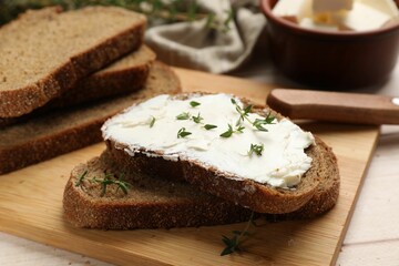 Fresh bread with butter, thyme and knife on light table, closeup