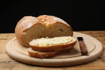 Fresh bread with butter and knife on wooden table, closeup