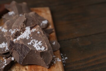 Pieces of chocolate with salt on wooden table, closeup. Space for text