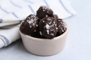 Tasty chocolate candies with salt in bowl on light table, closeup