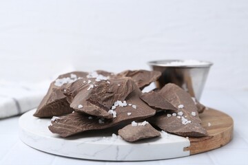 Pieces of tasty chocolate with salt on white tiled table, closeup