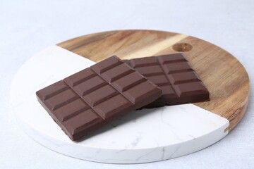 Pieces of delicious dark chocolate bar on light table, closeup
