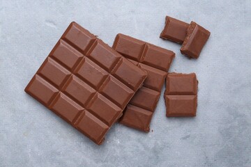 Pieces of delicious milk chocolate on grey table, top view