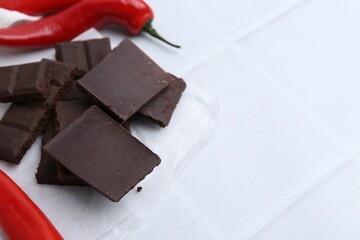 Pieces of chocolate with chili peppers on white table, closeup. Space for text