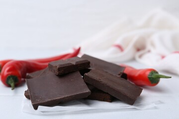 Pieces of chocolate with chili peppers on white table, closeup