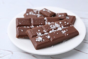 Pieces of chocolate with salt on white table, closeup