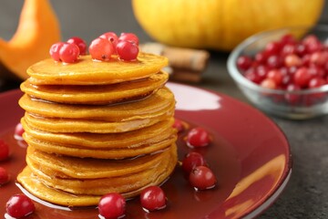 Tasty pumpkin pancakes with cranberries and honey on table, closeup