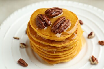 Tasty pumpkin pancakes with nuts and honey on plate, closeup