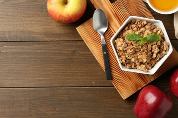 Tasty apple crisp in bowl, fresh fruits, honey and spoon on wooden table, flat lay. Space for text