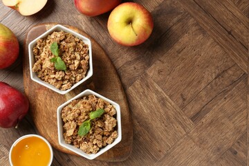 Tasty apple crisp in bowls, fresh fruits and honey on wooden table, flat lay. Space for text