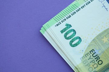 Big amount of one hundred euro money bills on lilac background