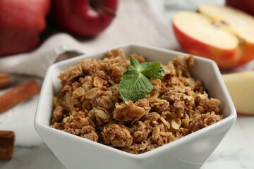 Tasty apple crisp in bowl and fresh fruits on light table, closeup