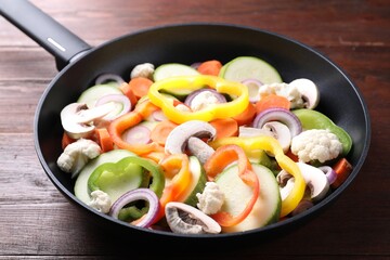 Frying pan with mix of vegetables and mushrooms on wooden table, closeup