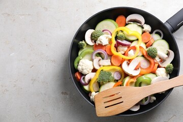 Frying pan with mix of vegetables, mushrooms and slotted turner on light grey table, top view. Space for text