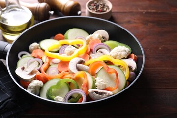 Frying pan with mix of vegetables and mushrooms on wooden table, closeup