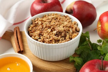 Delicious apple crisp in bowl, fresh fruits, mint, honey and cinnamon stick on table, closeup