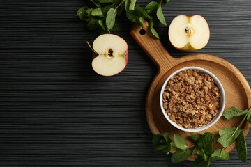 Delicious apple crisp in bowl, fresh fruits and mint on black textured table, flat lay. Space for text