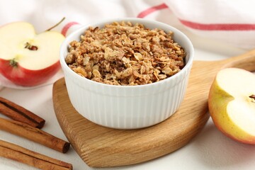 Delicious apple crisp in bowl, fresh fruits and cinnamon sticks on white table, closeup