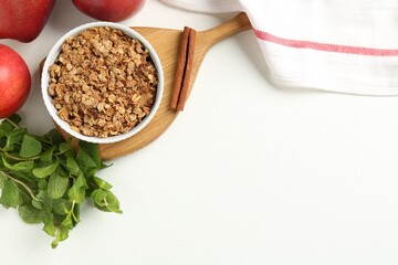 Delicious apple crisp in bowl, fresh fruits, mint and cinnamon stick on white table, flat lay....