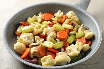 Frying pan with vegetables on light textured table, closeup