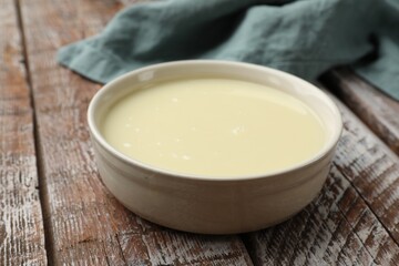 Condensed milk in bowl on wooden table, closeup
