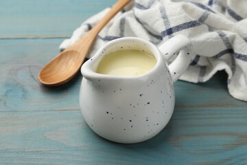 Condensed milk in jug and spoon on light blue wooden table, closeup
