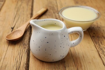 Condensed milk and spoon on wooden table, closeup