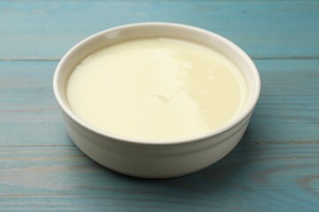 Condensed milk in bowl on light blue wooden table, closeup