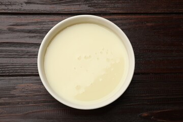 Condensed milk in bowl on wooden table, top view
