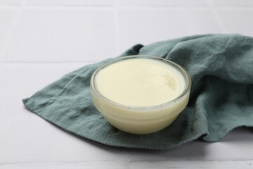 Tasty condensed milk in bowl and towel on white tiled table, closeup