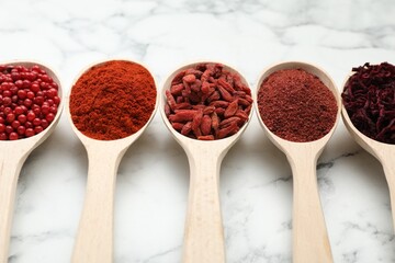Different aromatic spices in spoons on white marble table, closeup