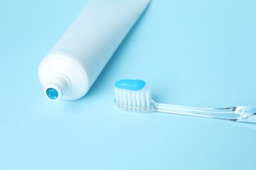 Toothbrush with toothpaste and tube on light blue background