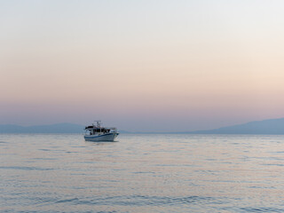 A serene evening unfolds as a fishing boat quietly drifts across calm waters. Soft hues of dusk reflect on the surface, highlighting the peacefulness of the moment.