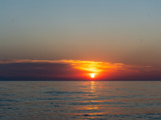 A stunning sunset unfolds over the calm ocean, painting the sky with shades of orange and purple. Gentle waves reflect the vibrant colors as the sun descends on the horizon.