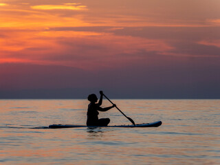 A person paddles thoughtfully on calm waters during a stunning sunset, casting a silhouette against vibrant clouds. The peaceful moment captures the essence of adventure.