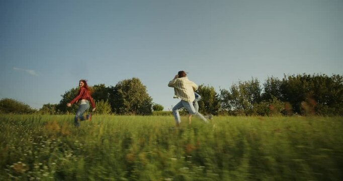 Three young friends are having fun and running around the field on a sunny summer day. Holidays in the countryside
