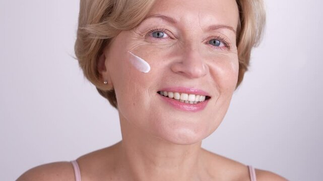 A radiant woman in her 50s posing for a portrait and applying face cream. Anti-aging skincare rituals, self-love and wellness. 4k high res