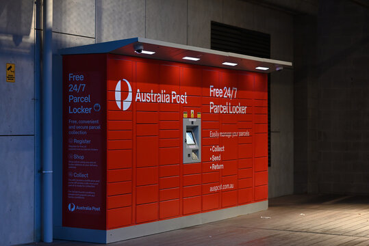 Red Australia Post parcel lockers illuminated at night, with surveillance cameras and warning sign nearby