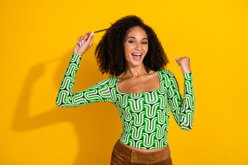 Joyful young woman in green top with curly hair and yellow background, expressing happiness and...